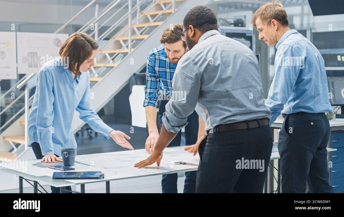 Dans le centre d'ingénierie industrielle : divers groupes d'ingénieurs et de techniciens réunis autour de la table démêle les feuilles de conception de moteur Banque D'Images