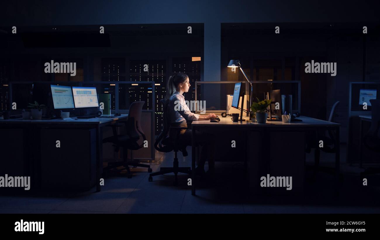 Travailler tard dans la nuit au bureau : femme d'affaires utilise l'ordinateur de bureau, analyse, utilisation de documents, résolution de problèmes, finition de projet important Banque D'Images