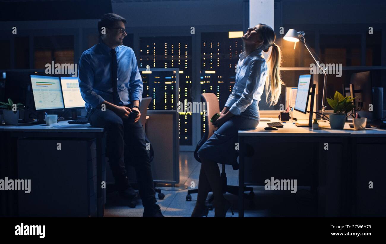 Tard dans la nuit dans le bureau de l'entreprise deux jeunes professionnels discutant amical, échanger des nouvelles, parler d'emploi, flirter Banque D'Images