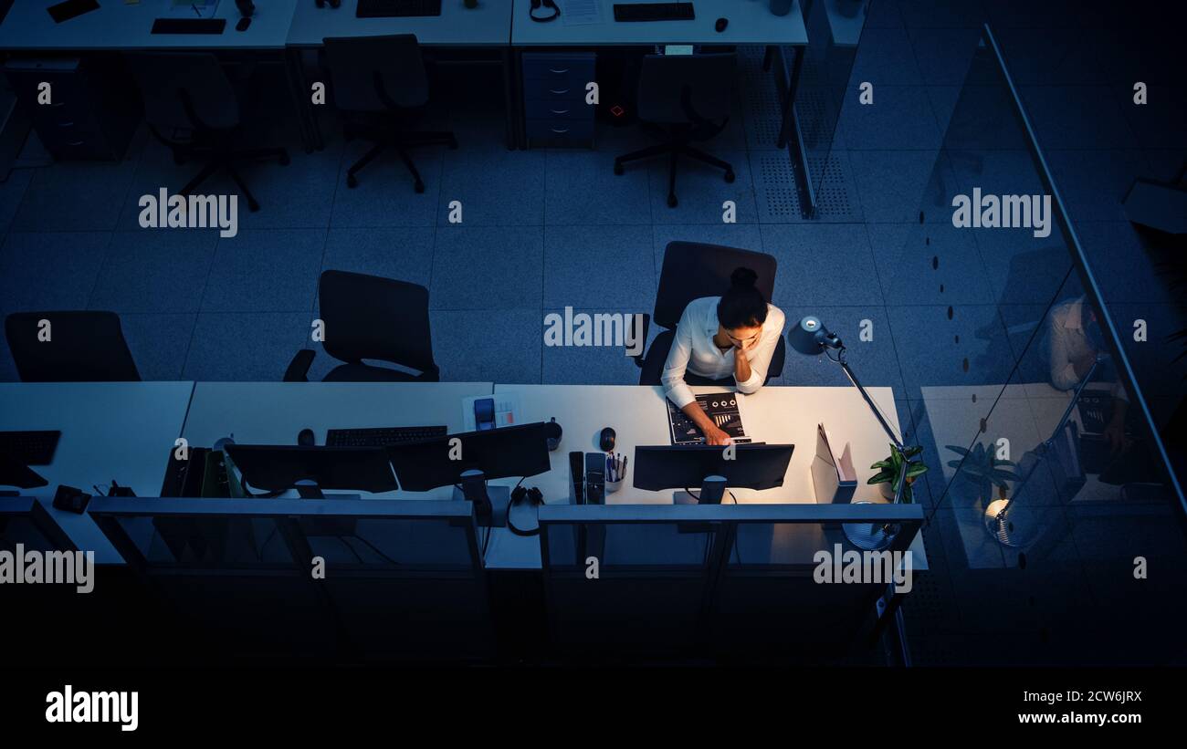 Travailler tard dans la nuit au bureau : femme d'affaires utilisant un ordinateur de bureau, analyser, utiliser des documents, résoudre des problèmes, terminer le projet. Angle élevé Banque D'Images