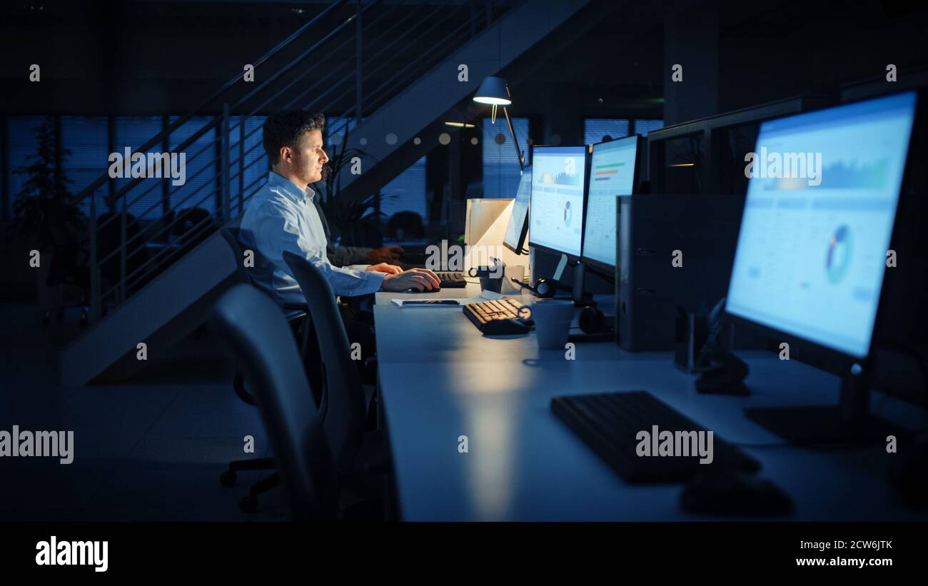 Travailler tard dans la nuit au bureau : l'homme d'affaires utilise un ordinateur de bureau, analyse, utilisation de documents, résolution de problèmes, finition de projet important Banque D'Images