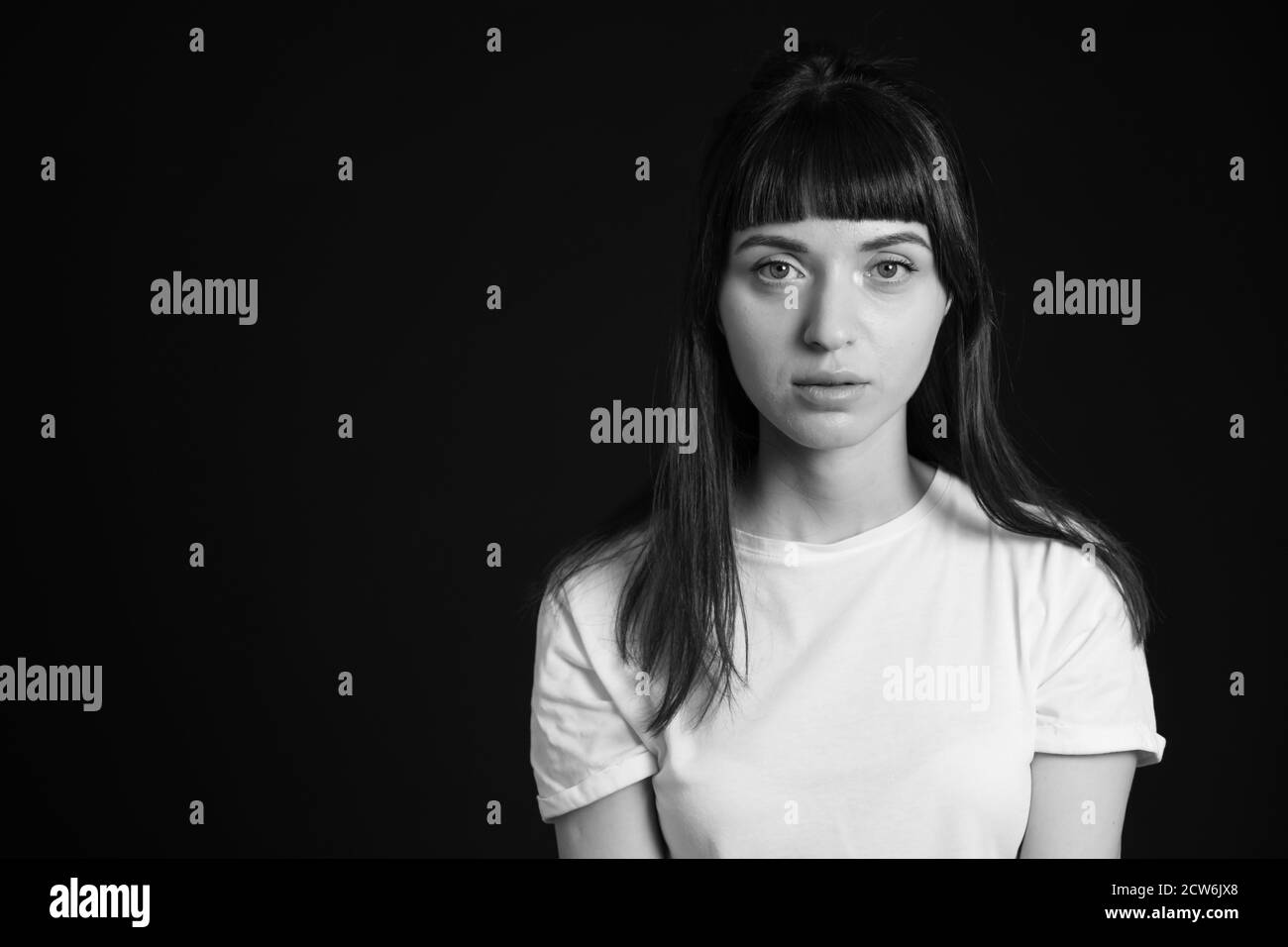 Portrait studio d'une jolie femme brune dans un t-shirt blanc, sur fond noir Uni, regardant l'appareil photo Banque D'Images