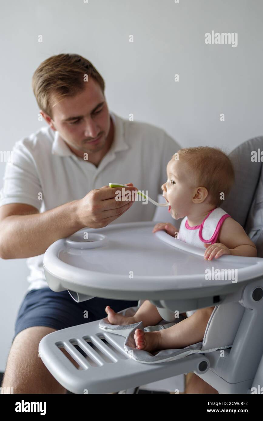 Père nourrissant bébé fille avec une cuillère dans une chaise haute Banque D'Images