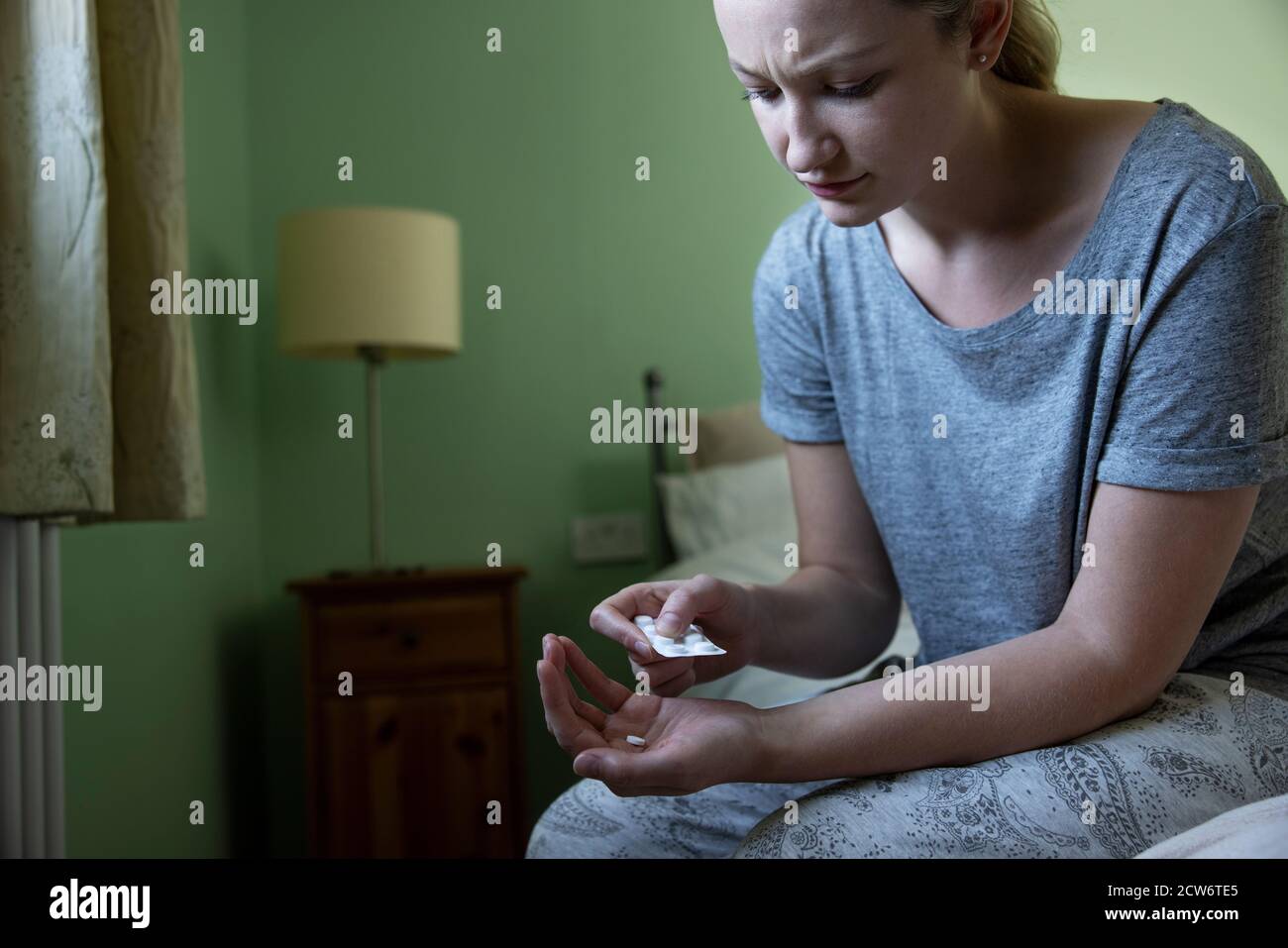 Femme assise sur le lit portant un pyjama prenant des médicaments Banque D'Images