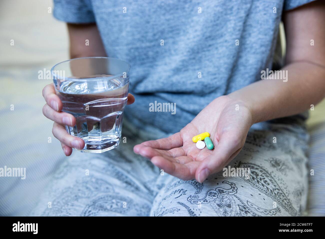 Gros plan d'une femme assise sur un lit portant un pyjama Médicament avec un verre d'eau Banque D'Images