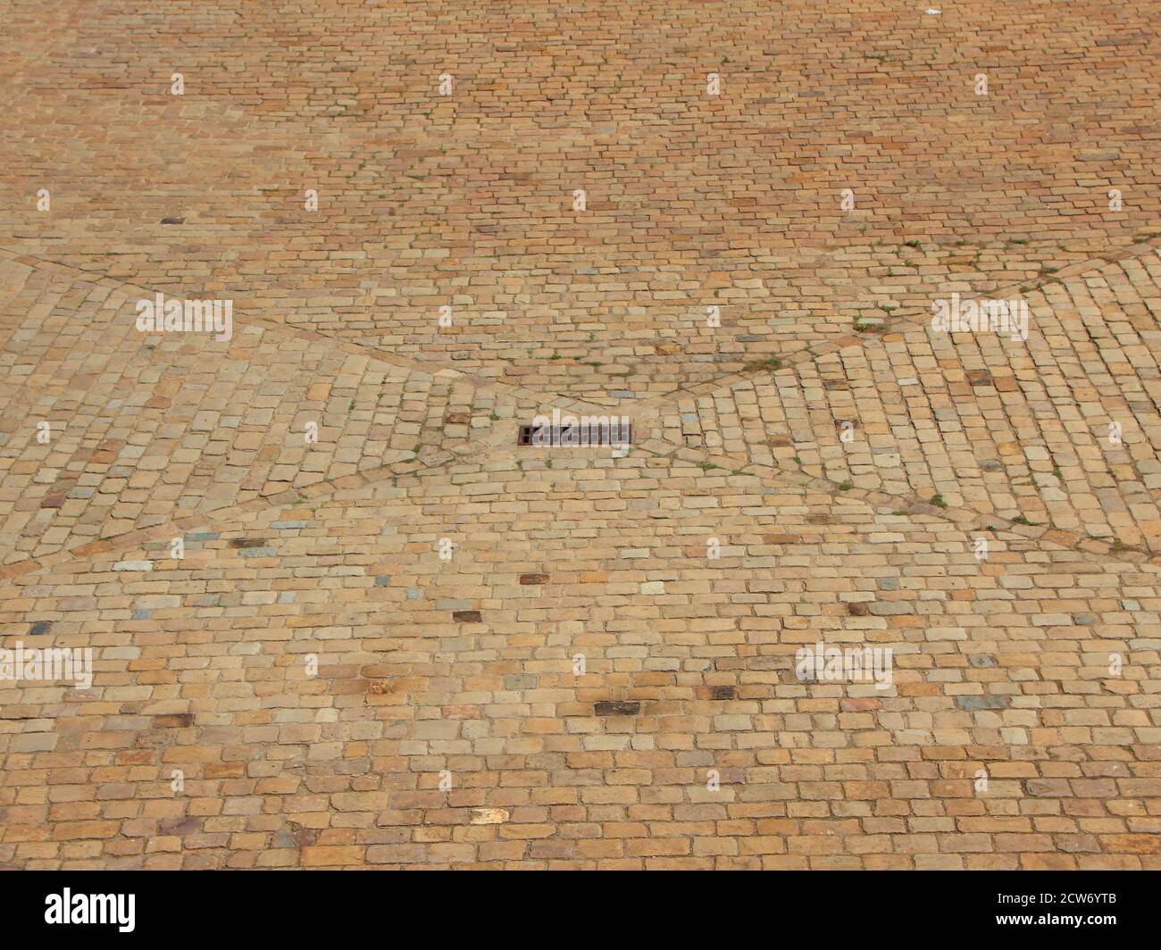 Grille métallique de drainage à la pluie entourée de briques brunes au centre de la place de la ville. Les briques sont dans un modèle géométrique entourant le drain. Banque D'Images
