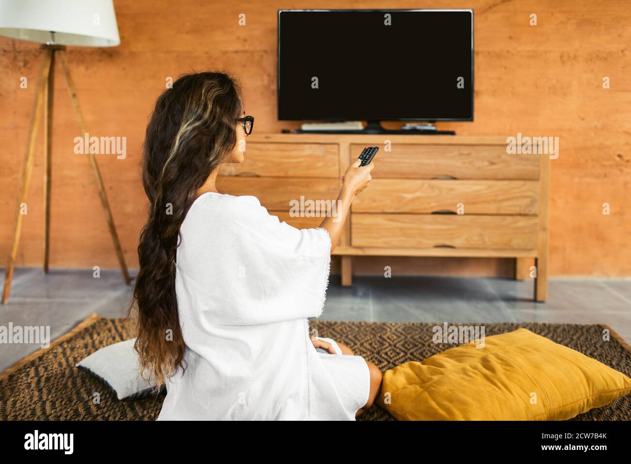 Divertissement à la maison, dépendance à la télévision. Restez à la maison. Femme changer de chaîne et regarder la télévision. Vue de derrière, personne méconnaissable. Banque D'Images