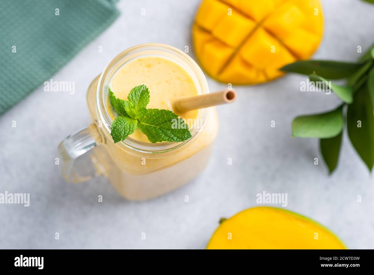 Smoothie mangue dans un pot en verre avec paille de bambou écologique décoration avec feuilles de menthe sur fond de béton gris Banque D'Images