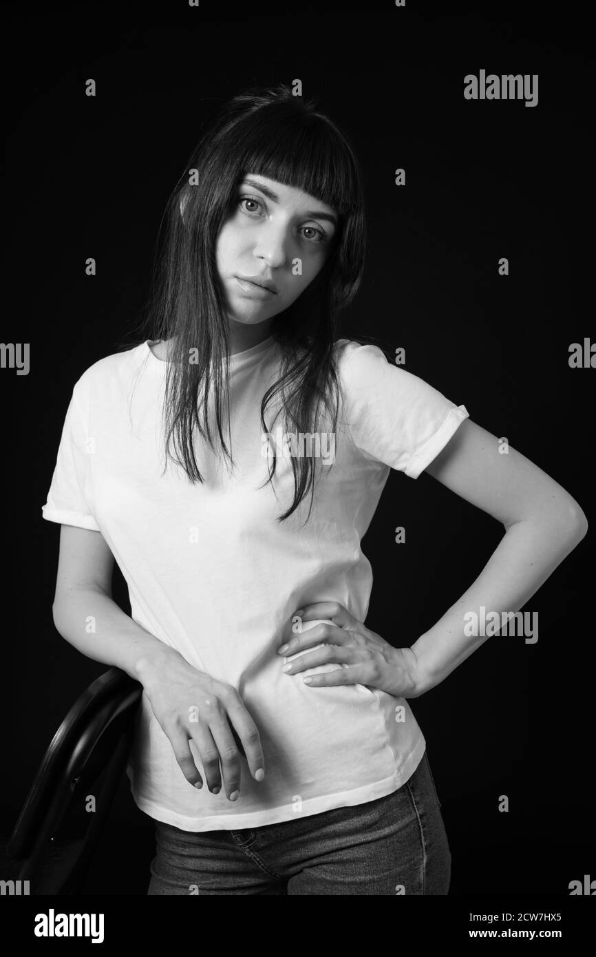 Portrait studio d'une jolie femme brune dans un t-shirt blanc, sur fond noir Uni, regardant l'appareil photo Banque D'Images