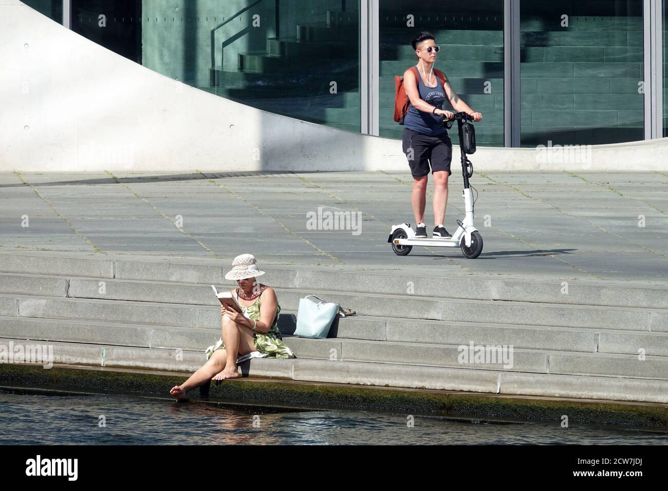 Touristes berlinois une femme sur un scooter électrique et une autre femme sur la rive de la Spree lit un livre, Allemagne, femme du tourisme lisant un livre dehors Banque D'Images