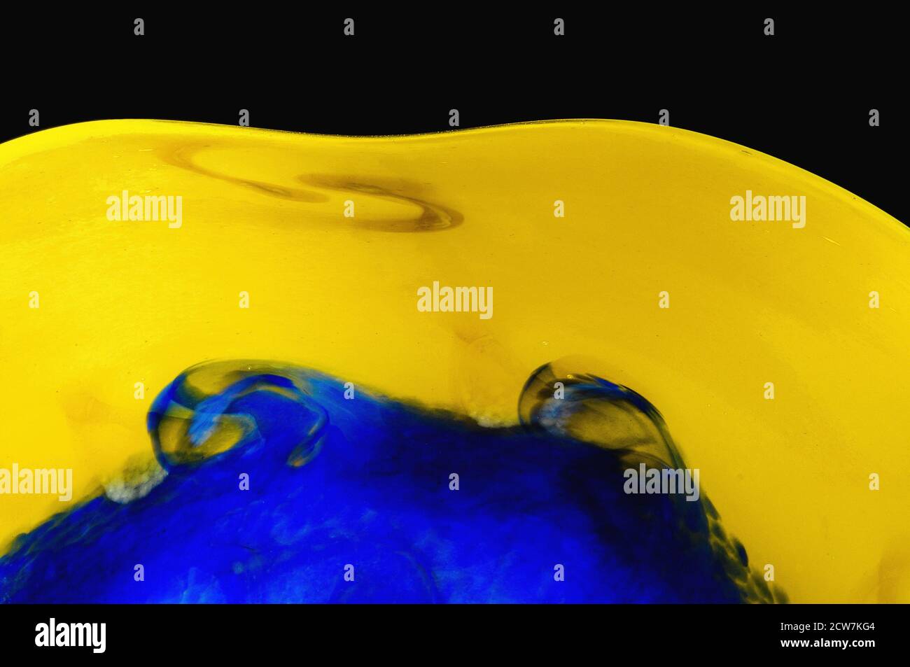 Le bord extérieur jaune ondulant d'un bol de fruits coloré contraste avec le bleu tourbillonnant en son centre dans ce bel exemple de verre d'art contemporain soufflé français créé par le maître «volant de verre» Pascal Guernic dans son atelier de studio à Monpazier, Dordogne, Nouvelle-Aquitaine, sud-ouest de la France. Banque D'Images