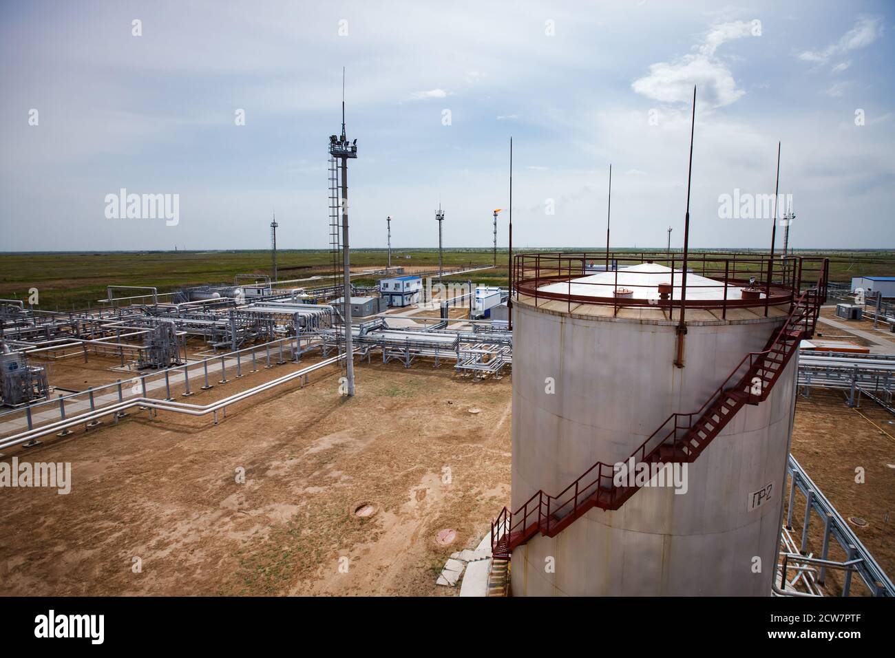 Gisement de pétrole de Zhaik-Munai, Kazakhstan. Usine de raffinerie de pétrole dans les sables. Réservoir de stockage de pétrole, mâts, pipelines. Torche à gaz orange en arrière-plan. Ciel bleu Banque D'Images