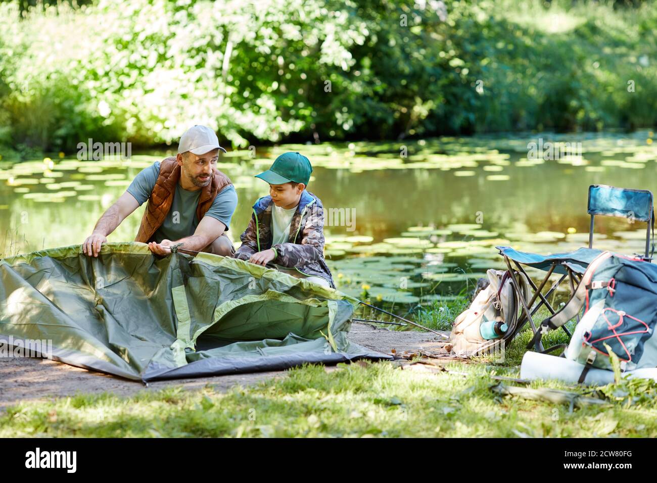 Portrait complet du père et du fils dressant la tente ensemble tout en appréciant le camping au bord du lac dans la forêt, espace de copie Banque D'Images