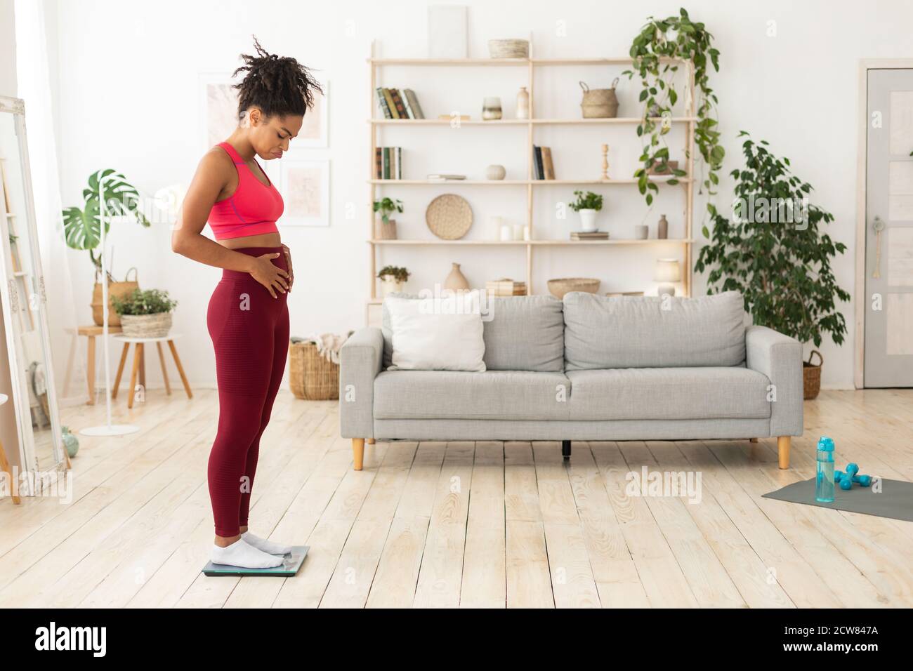 Malheureux Afro-américaine femme debout sur les balances de poids touchant Belly intérieur Banque D'Images