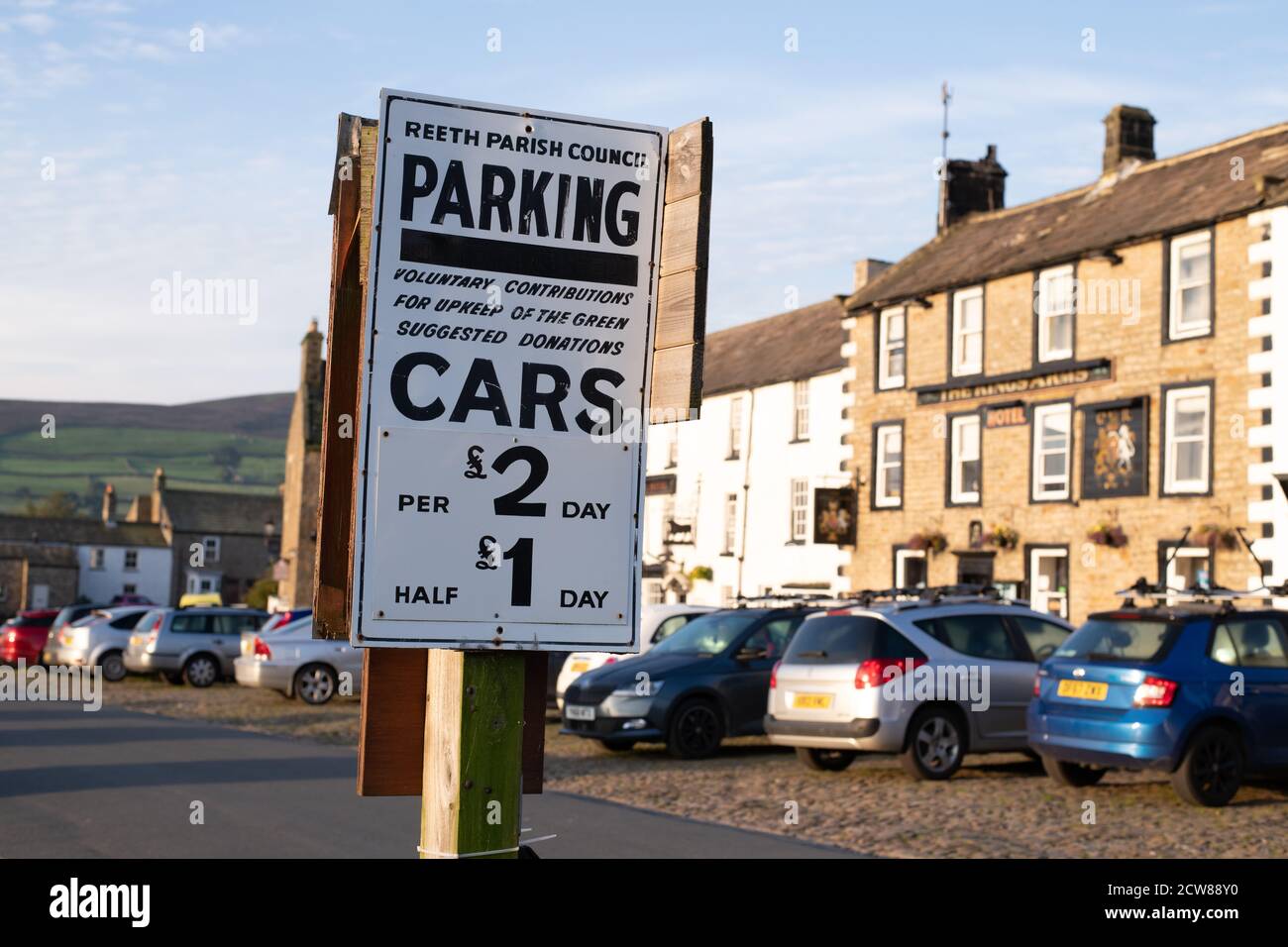 Voitures et panneau de parking demandant un paiement volontaire pour aider à l'entretien des Green, Reeth, Swaledale, Angleterre, Royaume-Uni Banque D'Images