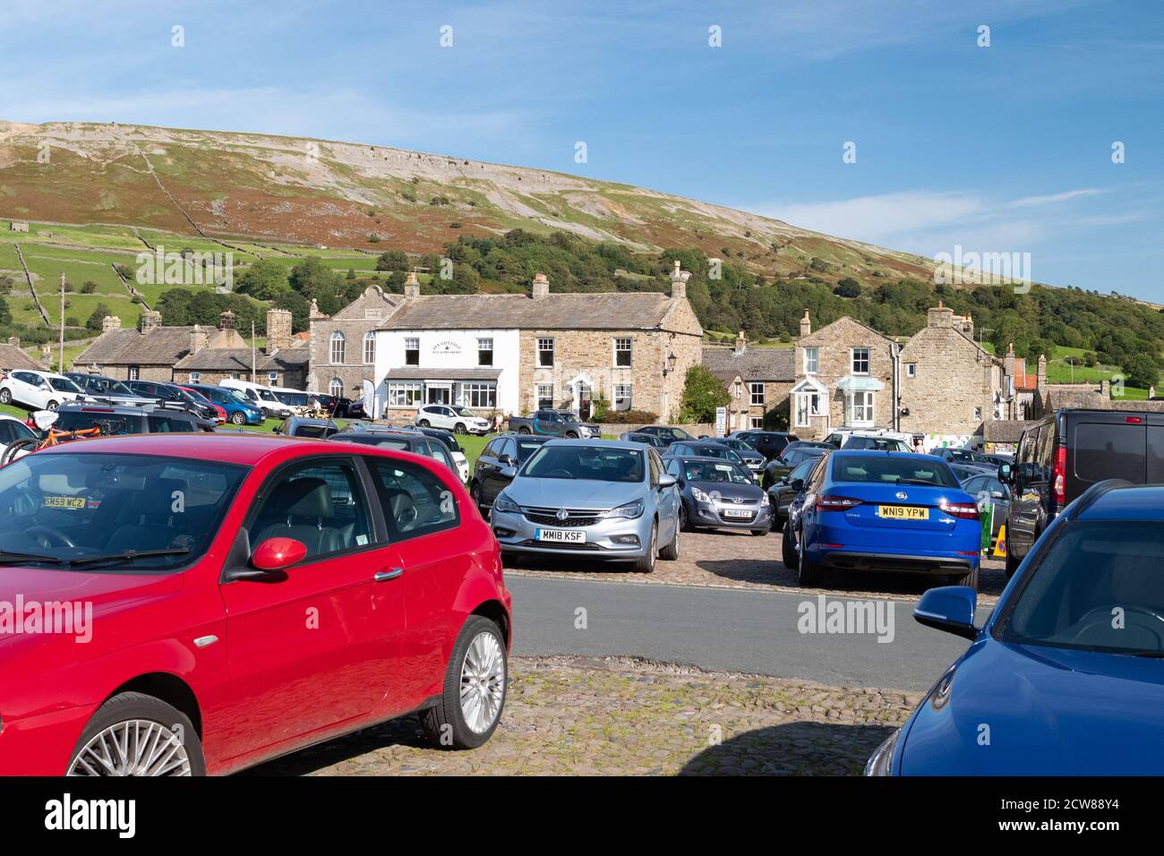 Voitures et parking sur galets et le village vert à Reeth, Swaledale, Angleterre, Royaume-Uni Banque D'Images