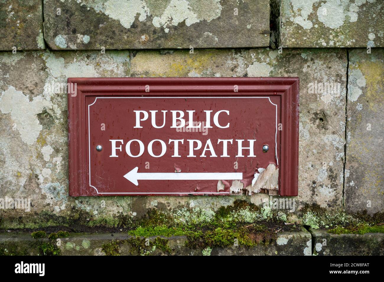 Dirigez-vous vers la vue d'un vieux panneau de chemin public en difficulté sur un vieux mur en pierre. Banque D'Images