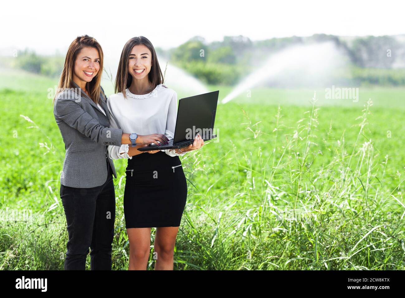 Femmes d'affaires avec un ordinateur portable dans un champ avec système d'irrigation agricole. Arroseurs d'eau en arrière-plan. Banque D'Images
