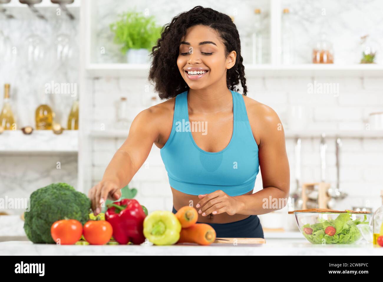 Jeune femme noire souriante préparant une salade de légumes Banque D'Images