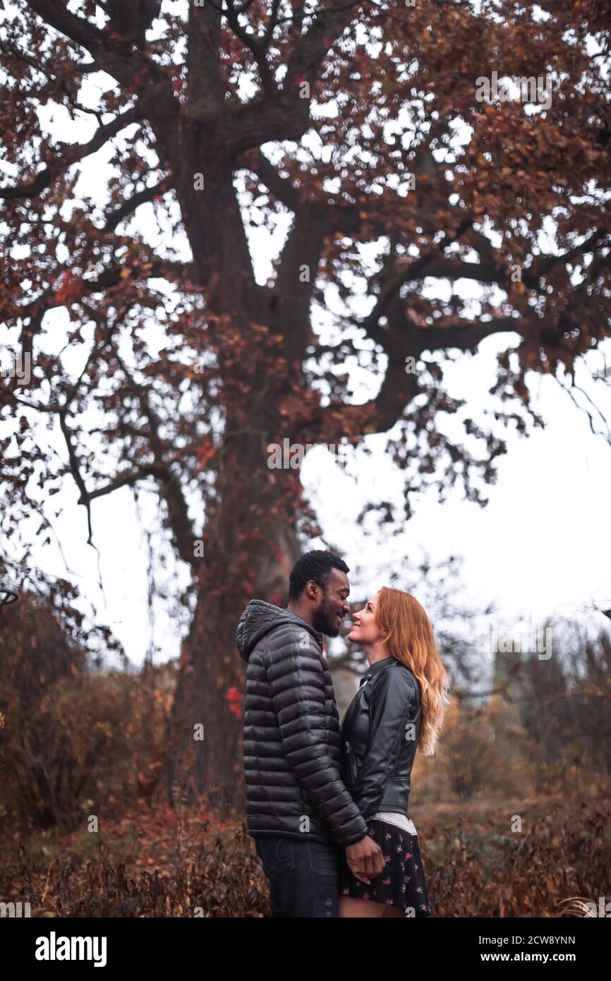 Couple interracial posant en automne feuilles fond, homme noir et femme blanc à tête rouge Banque D'Images