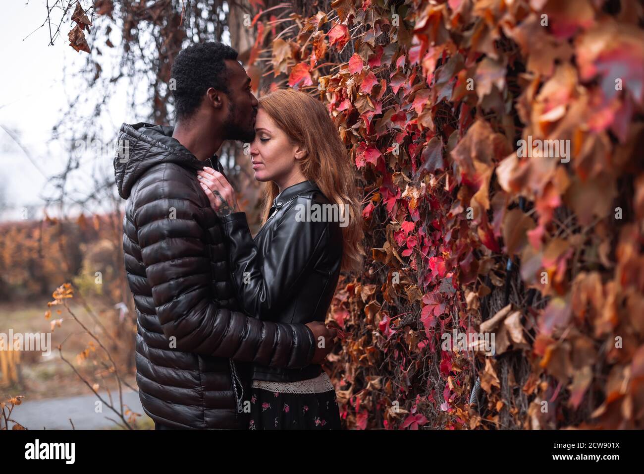 Couple interracial posant en automne feuilles fond, homme noir et femme blanc à tête rouge Banque D'Images