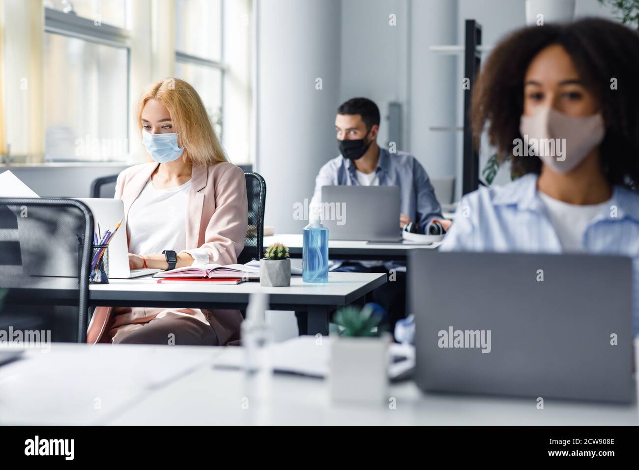 Bureau de travail moderne avec des travailleurs multiraciaux après la quarantaine. Concentrez-vous sur la bouteille avec antiseptique bleu sur le bureau du gestionnaire Banque D'Images