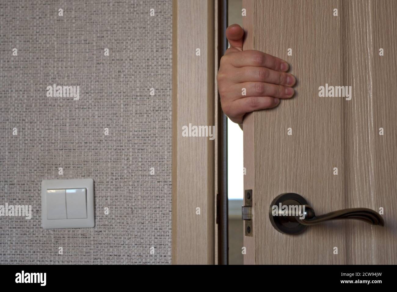 Main de la femme qui est derrière la porte, tenir la porte, l'ouvrir ou la fermer. Concept: Perturbation de la paix, invasion de la vie privée. Banque D'Images