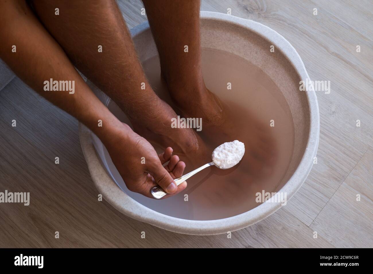 L'homme a mis une cuillère de bicarbonate de soude dans le bain avec de l'eau chaude pour ses pieds. Bain maison pour les pieds secs Banque D'Images