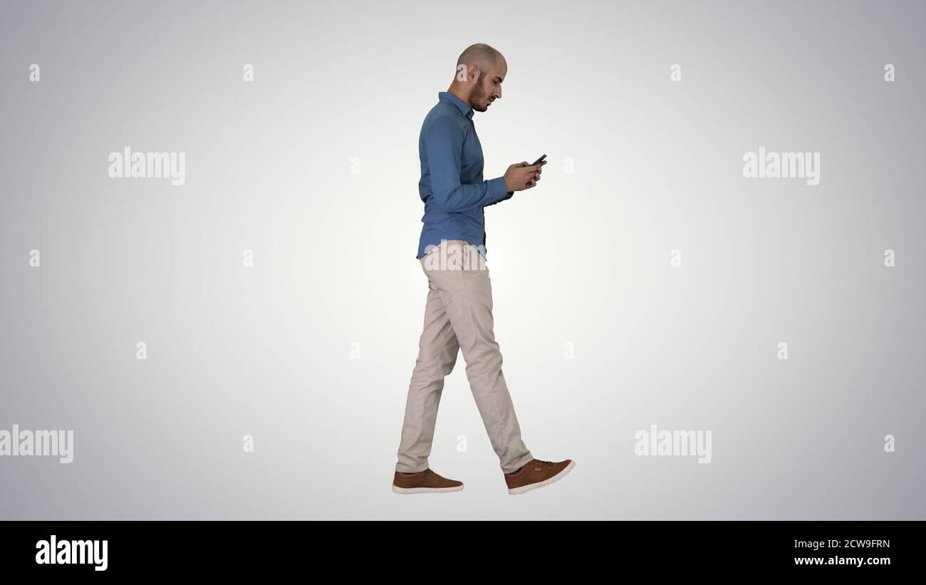 Jeune homme marchant et utilisant un téléphone sur fond dégradé. Banque D'Images