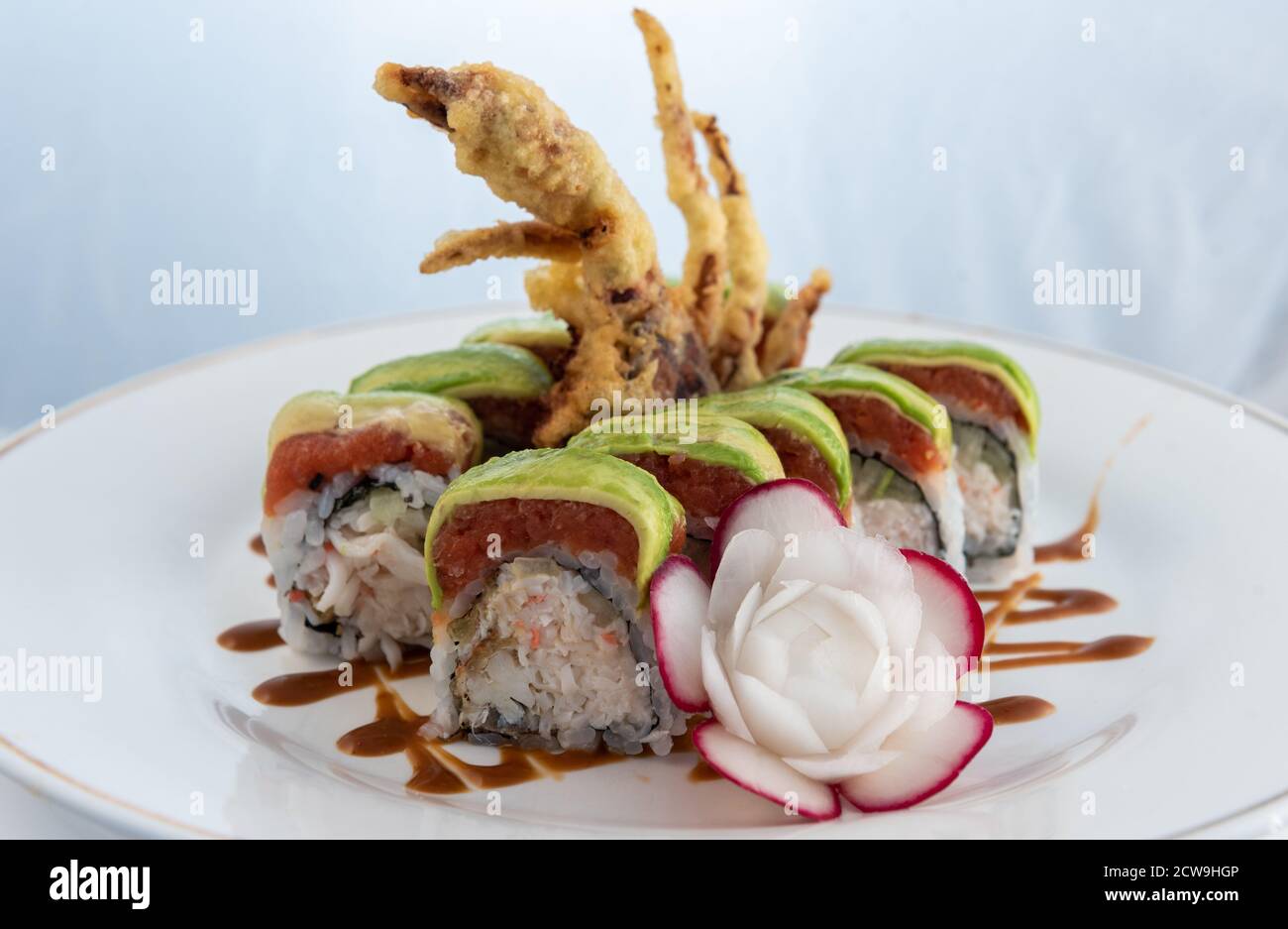 Thon épicé et tempura frits profonds disposés dans un rouleau de sushi avec une fleur de radis artistique délicatement présentée sur une assiette à manger. Banque D'Images