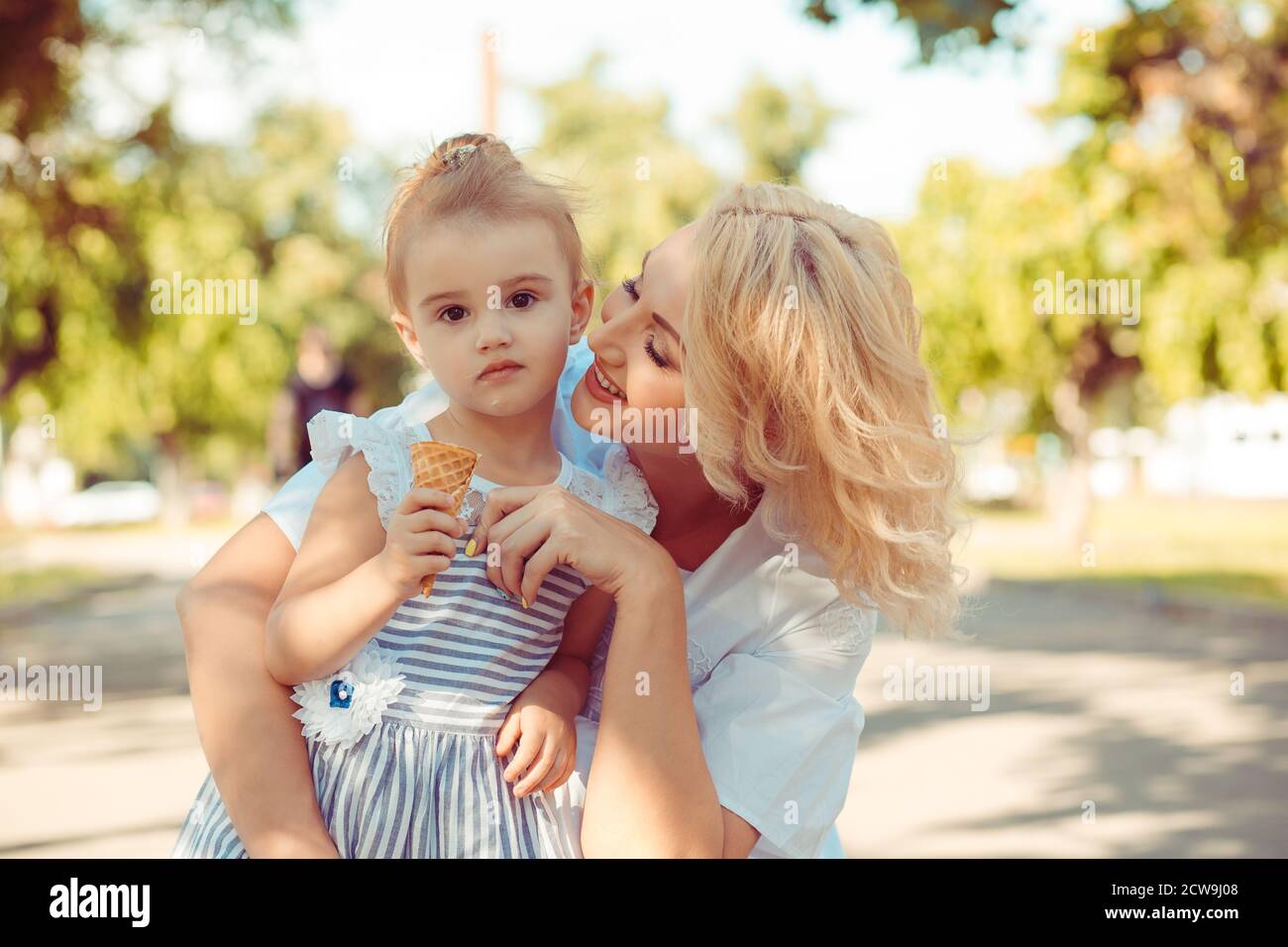 Femme prenant soin de regarder son enfant, la petite fille mange de la crème glacée et vous regarde la caméra souriant dans Spring Park. Le concept de famille amour de soins Banque D'Images