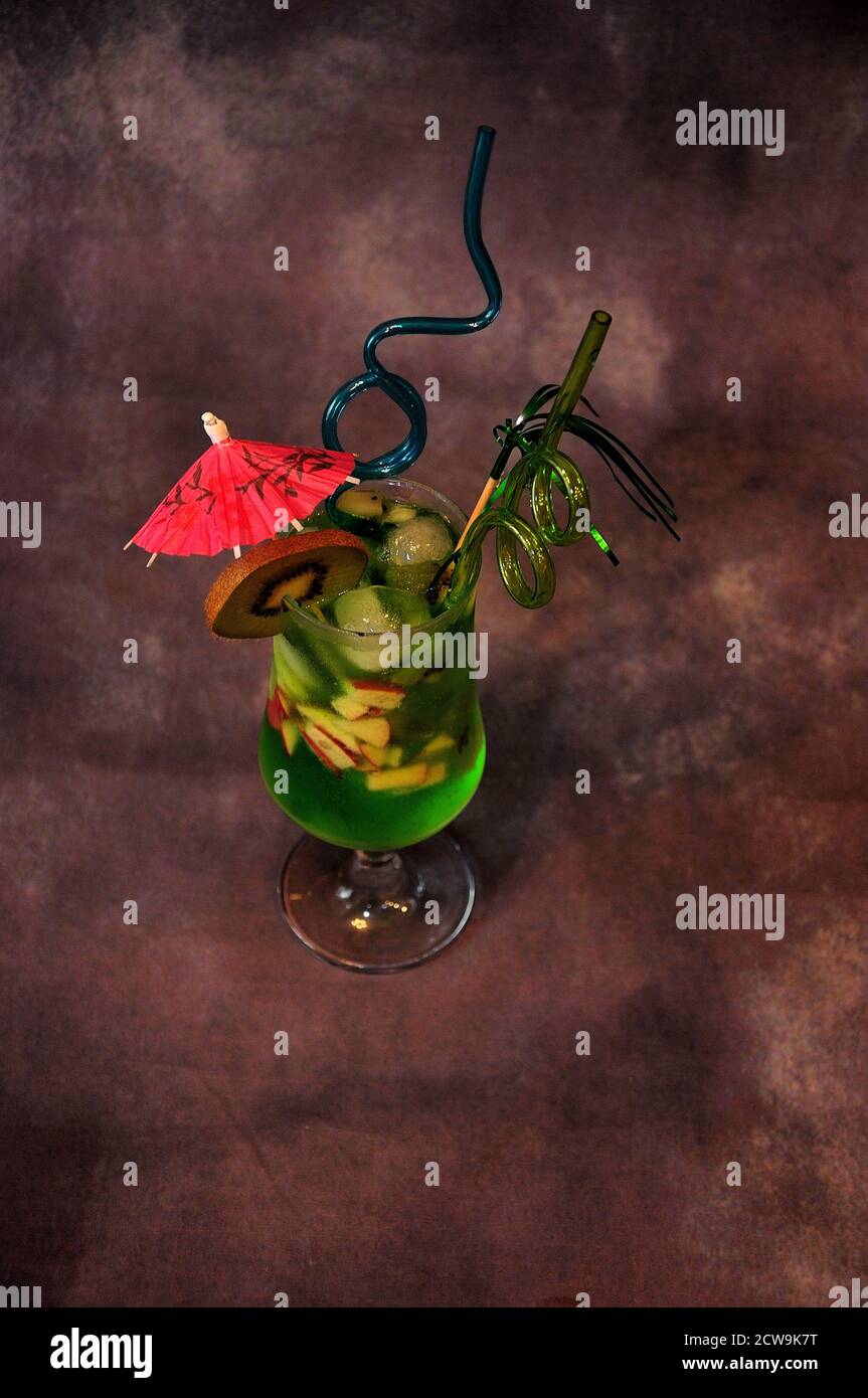 Un verre de jus à base de kiwi avec glace, morceaux de fruits, parapluie et pailles. Gros plan. Banque D'Images