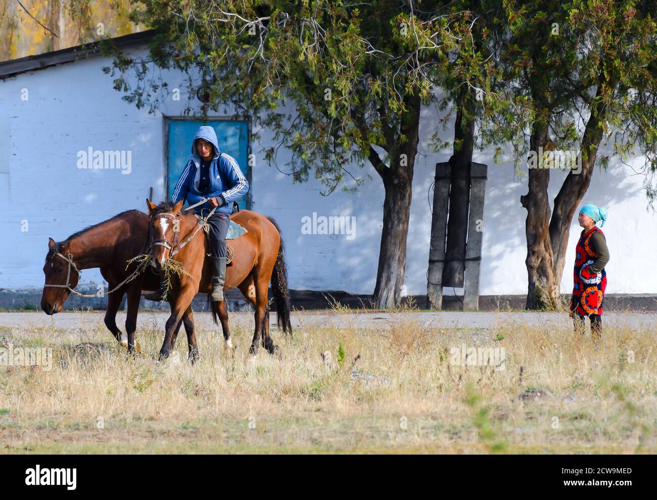 Homme de campagne d'âge moyen au Kirghizistan à cheval portant une veste bleue avec capuche. Equitation dans la zone rurale près de la région kirghize d'Issyk Kul. Banque D'Images