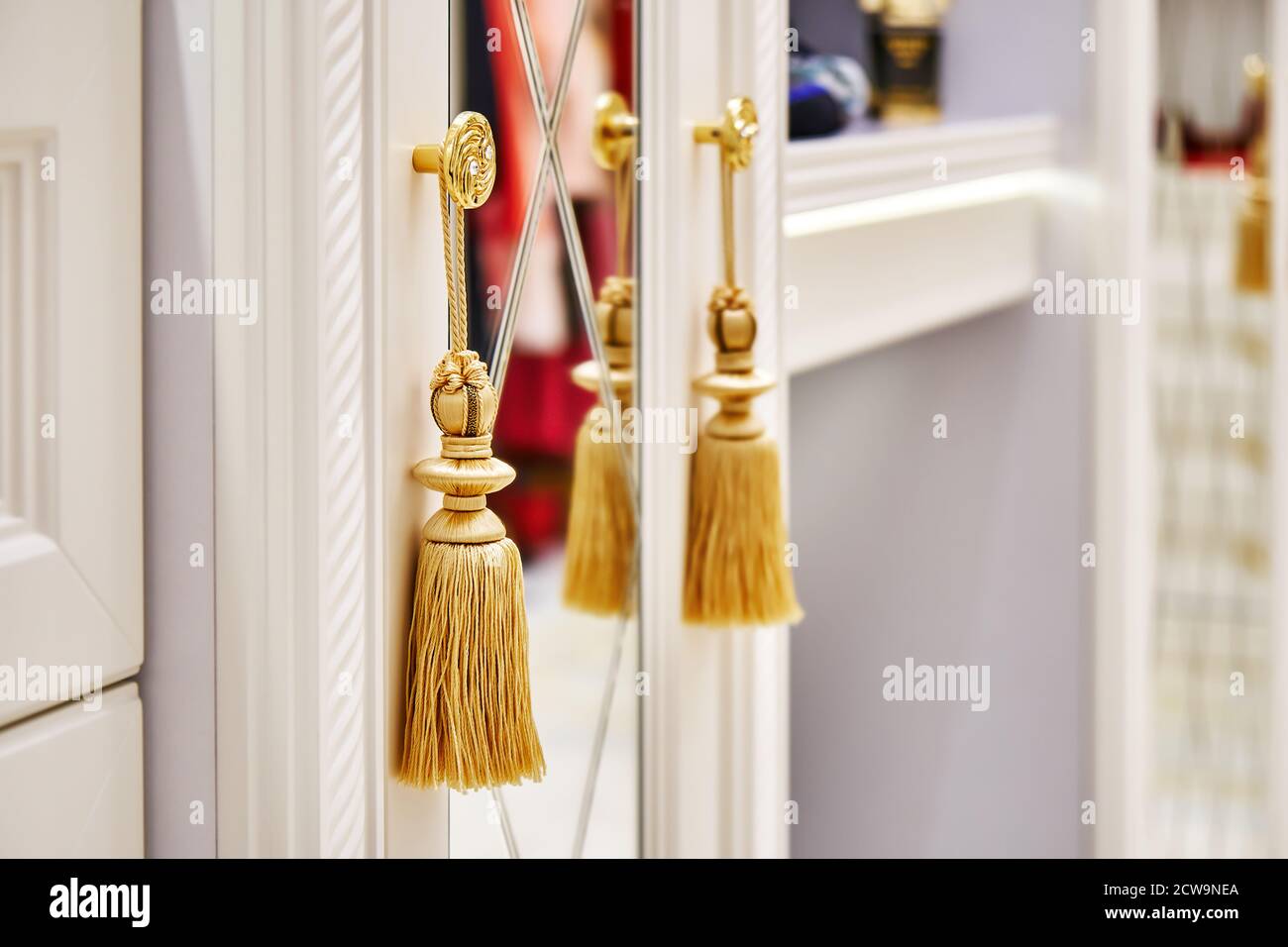 Détail de l'armoire blanche avec miroir et glands dorés suspendus sur les boutons dans le dressing Banque D'Images