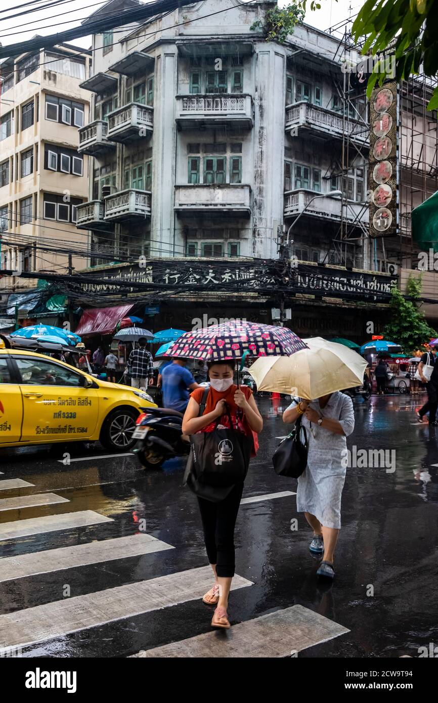 Les voyageurs se déplacent de l'autre côté de la rue avec des parasols alors qu'ils commencent un trajet pluvieux à la maison dans le quartier chinois de Bangkok. Banque D'Images