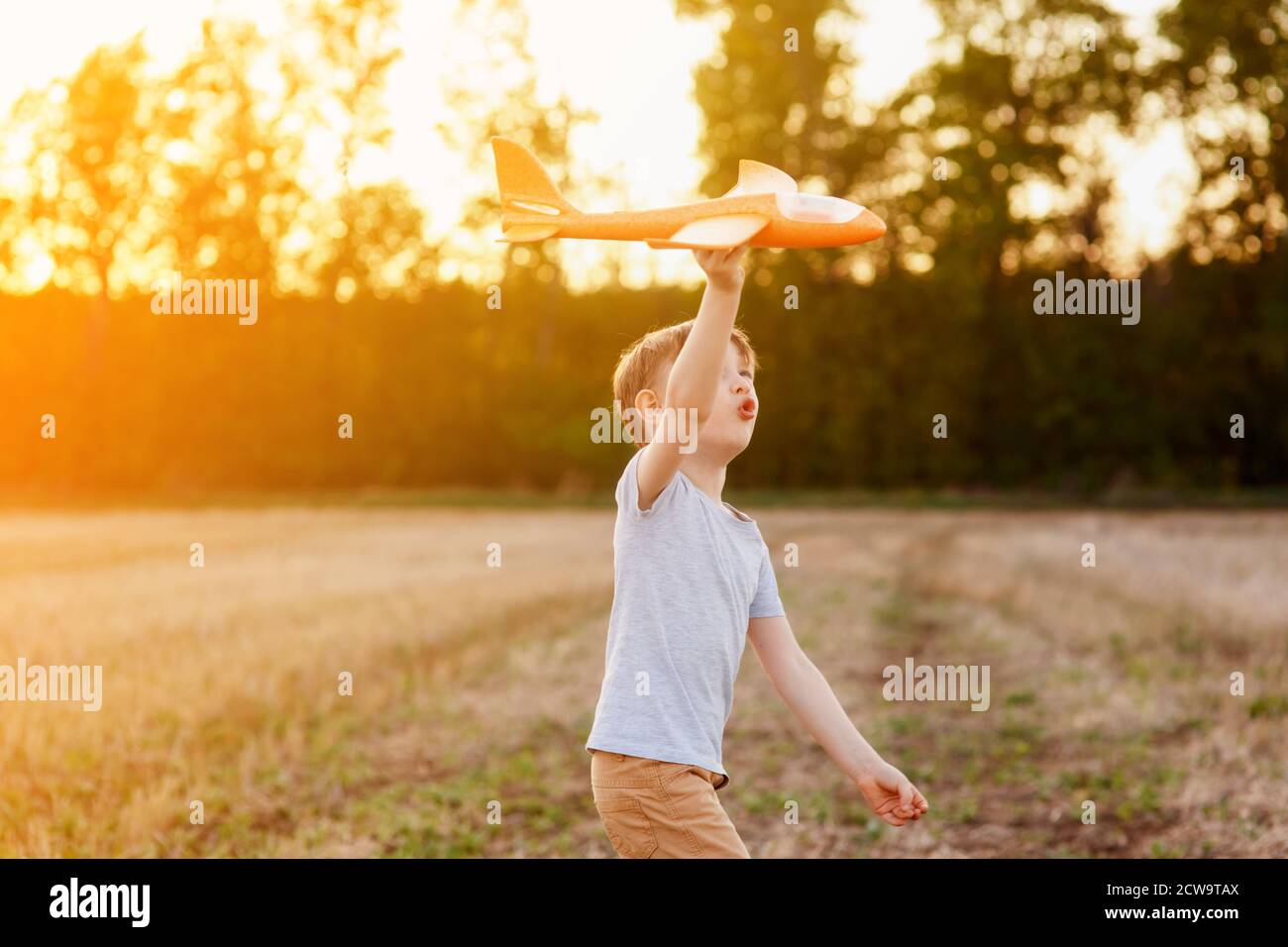 Un enfant heureux court avec un avion jouet sur un fond de coucher de soleil sur un champ. Le concept d'une famille heureuse. Rêves d'enfance Banque D'Images