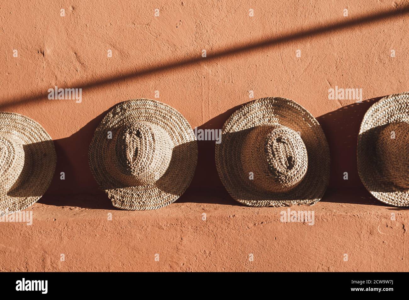 Chapeaux en osier sur fond de mur de couleur terre cuite au Maroc. Lumière  du soleil et ombres Photo Stock - Alamy