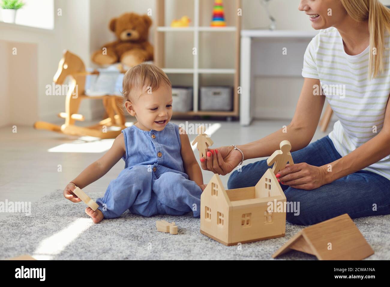 Joyeux jeune nounou et petit enfant jouant avec des blocs de bois dans une chambre confortable Banque D'Images