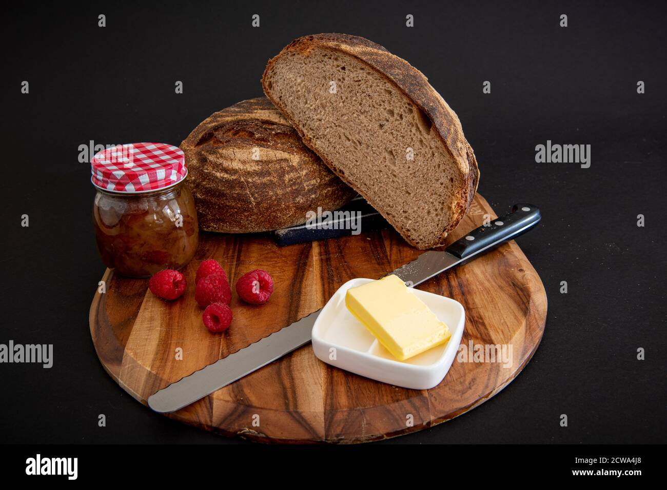 Pain de seigle sur une planche de bois avec beurre et framboises avec un arrière-plan sombre Banque D'Images