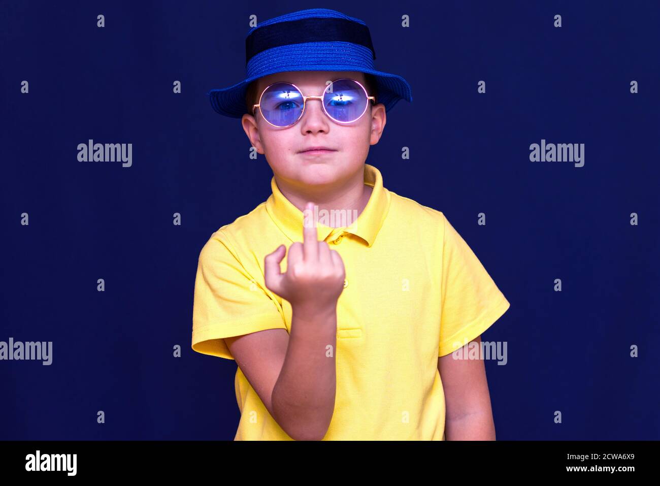 Jeune scolaire caucasien attrayant avec chapeau lunettes de soleil et t-shirt jaune montre le doigt du milieu.gros plan concept.Studio mur bleu. Banque D'Images