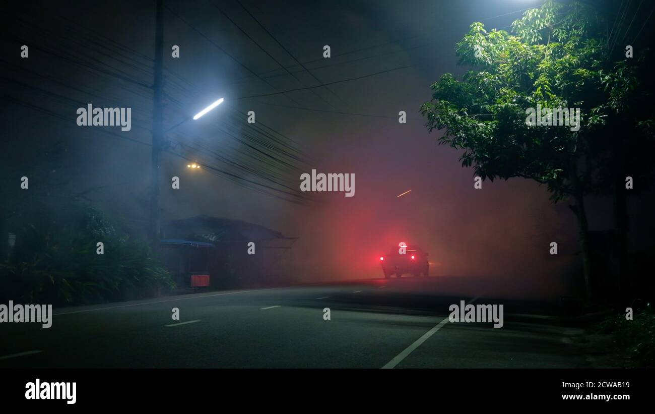 Le camion-pick-up se déplace dans le brouillard sur une route vide avec du rouge feu arrière en ville silencieuse Banque D'Images