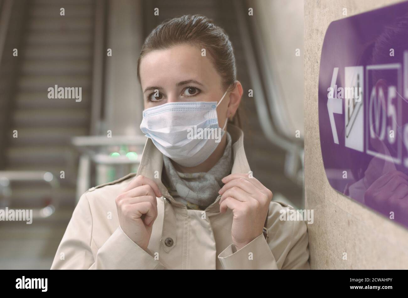 Fille avec un masque médical sur son visage et élevé mains dans le fond des escaliers roulants vides et une direction métro flèche Banque D'Images