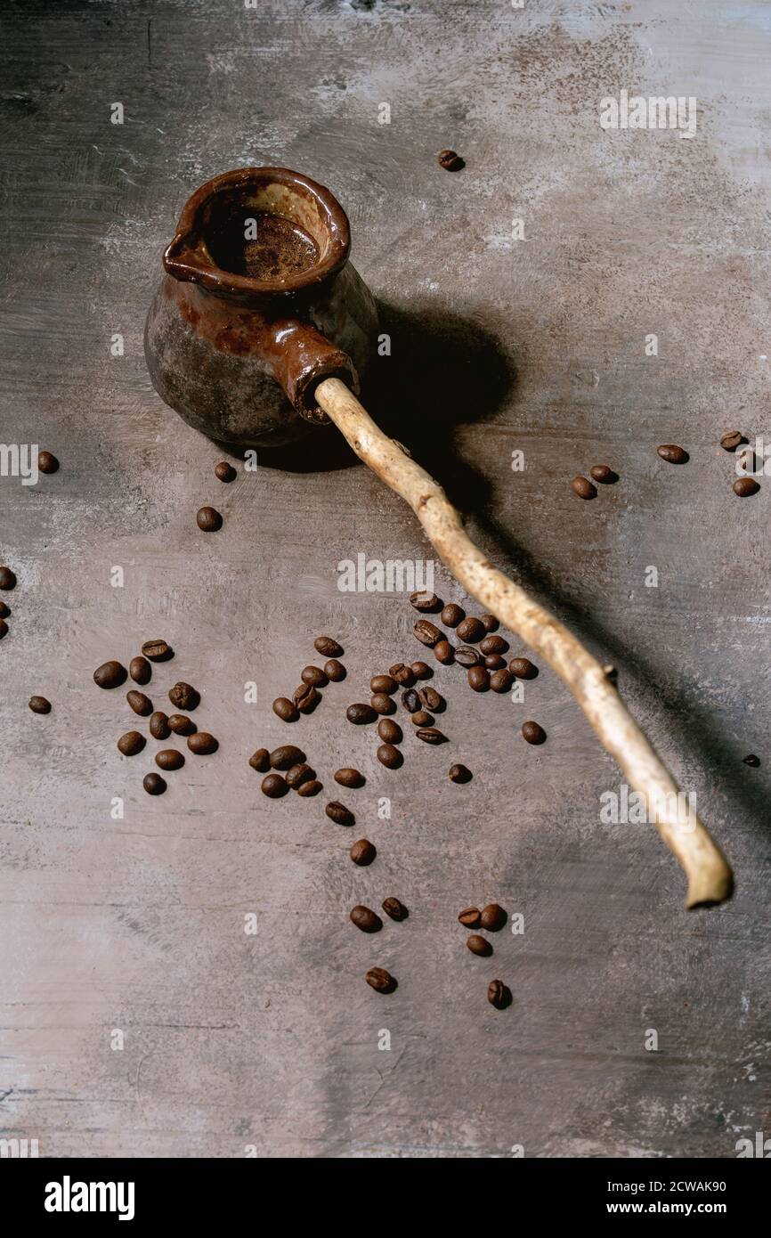 Café turc noir dans une cafetière artisanale en céramique avec une longue poignée en bois et des grains de café au-dessus. Fond de texture gris. Copier l'espace Banque D'Images