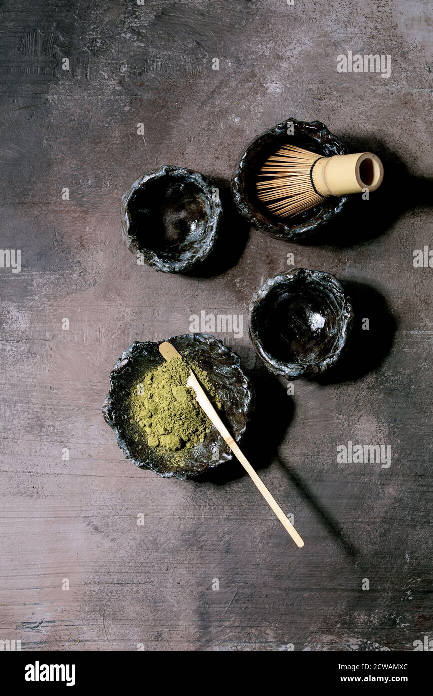 Poudre de thé vert matcha japonais dans un bol en céramique artisanale, deux tasses, fouet en bambou sur fond de texture sombre. Pose à plat, espace Banque D'Images