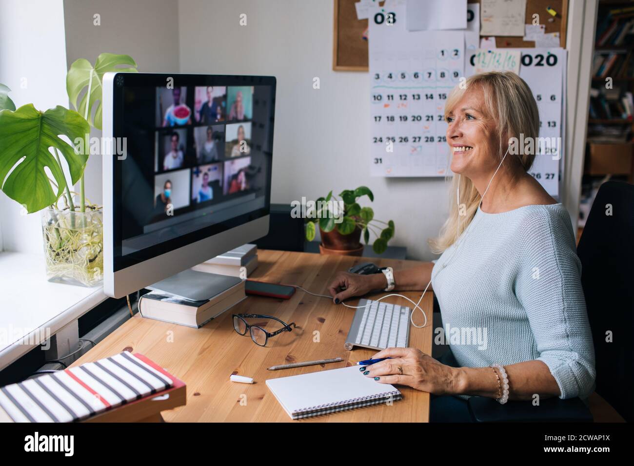 Femme mûre souriante ayant des appels vidéo via l'ordinateur le bureau à domicile. Vidéoconférence en ligne pour les réunions d'équipe depuis la maison. Femme d'affaires attirante Banque D'Images