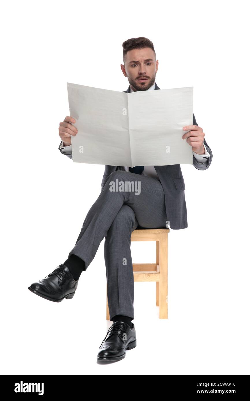 un jeune homme d'affaires choqué lisant le journal, assis isolé sur fond blanc, plein corps Banque D'Images