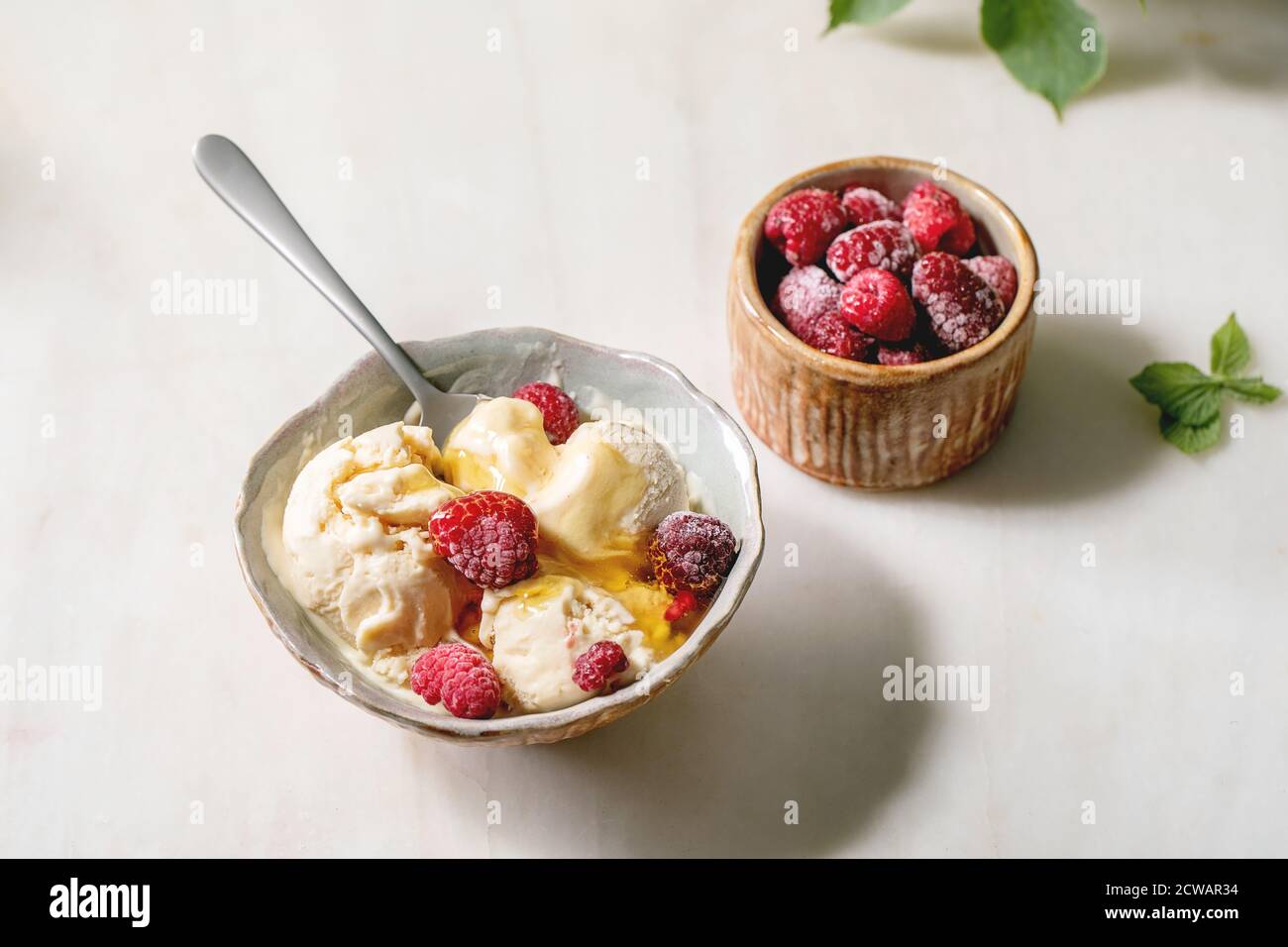Glace à la vanille au caramel fondu maison avec sirop et framboises congelées dans un bol en céramique placé sur une table en marbre blanc. Banque D'Images