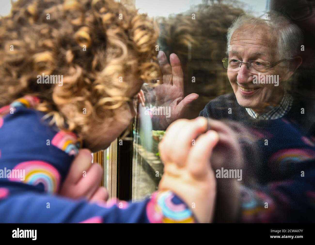 Lillian Joy âgée de deux ans regarde son grand-père Edward, âgé de 80 ans, à travers une fenêtre pendant que les réunions à l'intérieur sont interdites dans le quartier de Neath Port Talbot in Banque D'Images
