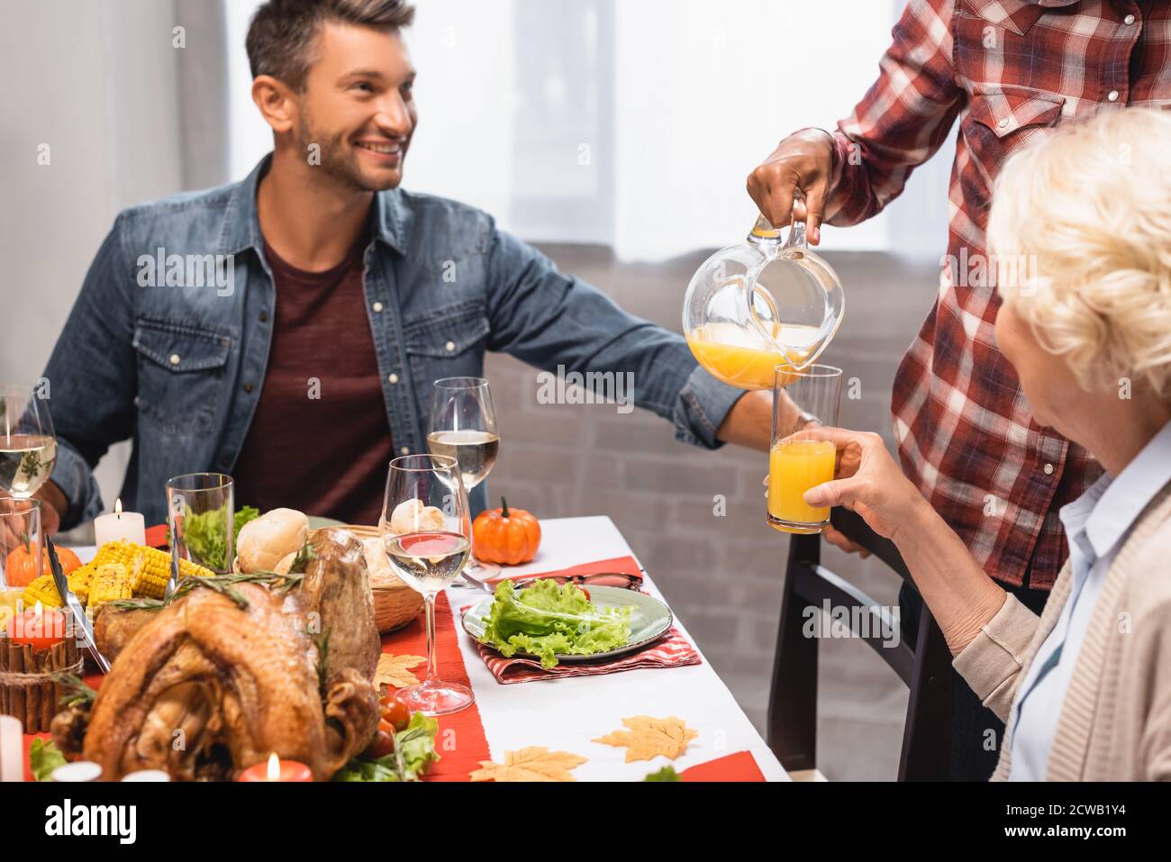 homme joyeux assis à table avec un dîner d'action de grâce pendant qu'africain une femme américaine verse du jus d'orange Banque D'Images