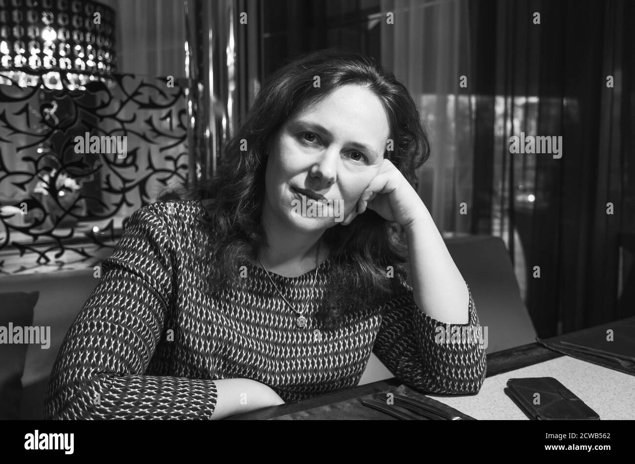 Femme européenne adulte assise dans un restaurant, portrait en gros plan noir et blanc avec mise au point sélective Banque D'Images